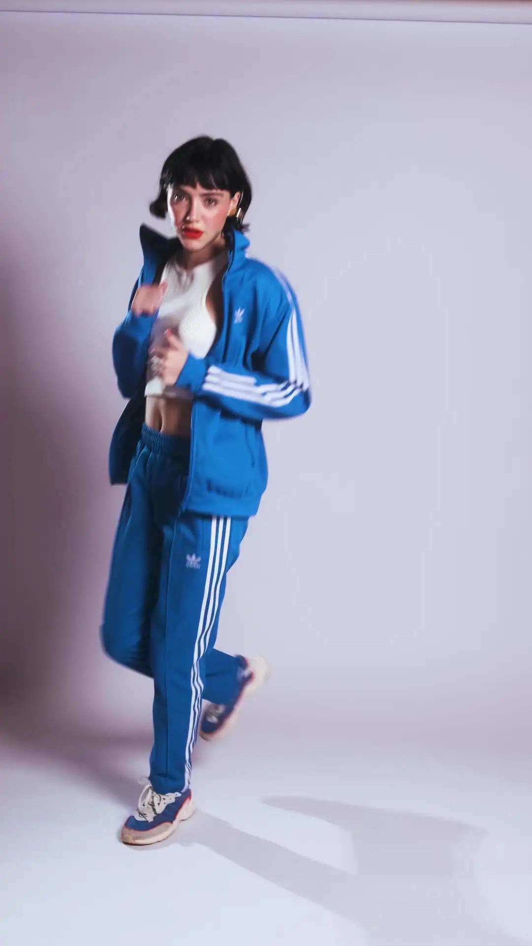 uma coisa meio perfomance, meio modas, meio indo correr.  #pratodosverem modelo aparece em ambiente interno e fundo neutro e veste em primeiro momento: calça e casaco adidas, na cor azul, e blusa branca. depois, casaco e short adidas, na cor vermelha, e blusa branca. 